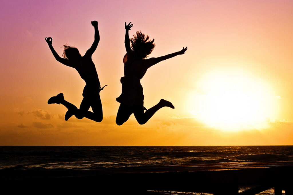 silhouette of two people jumping up in joy in front of sunset